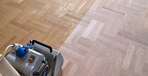 Une personne utilise une ponçeuse pour rénover un parquet en bois naturel, montrant le contraste avant et après ponçage.