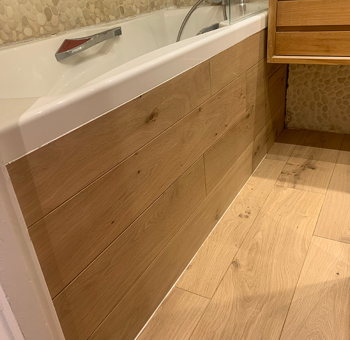 Salle de bain au sol en parquet bois naturel, dotée d'une baignoire avec revêtement assorti au sol, alliant style et confort pour un moment de détente.