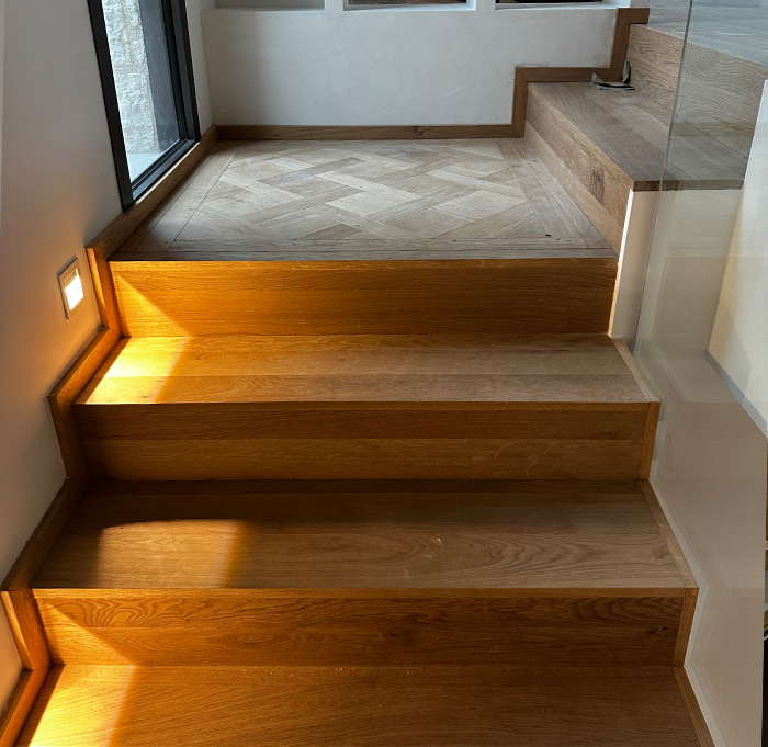 Une lumière éclaire un escalier en bois, soulignant son design élégant et sa chaleur naturelle.