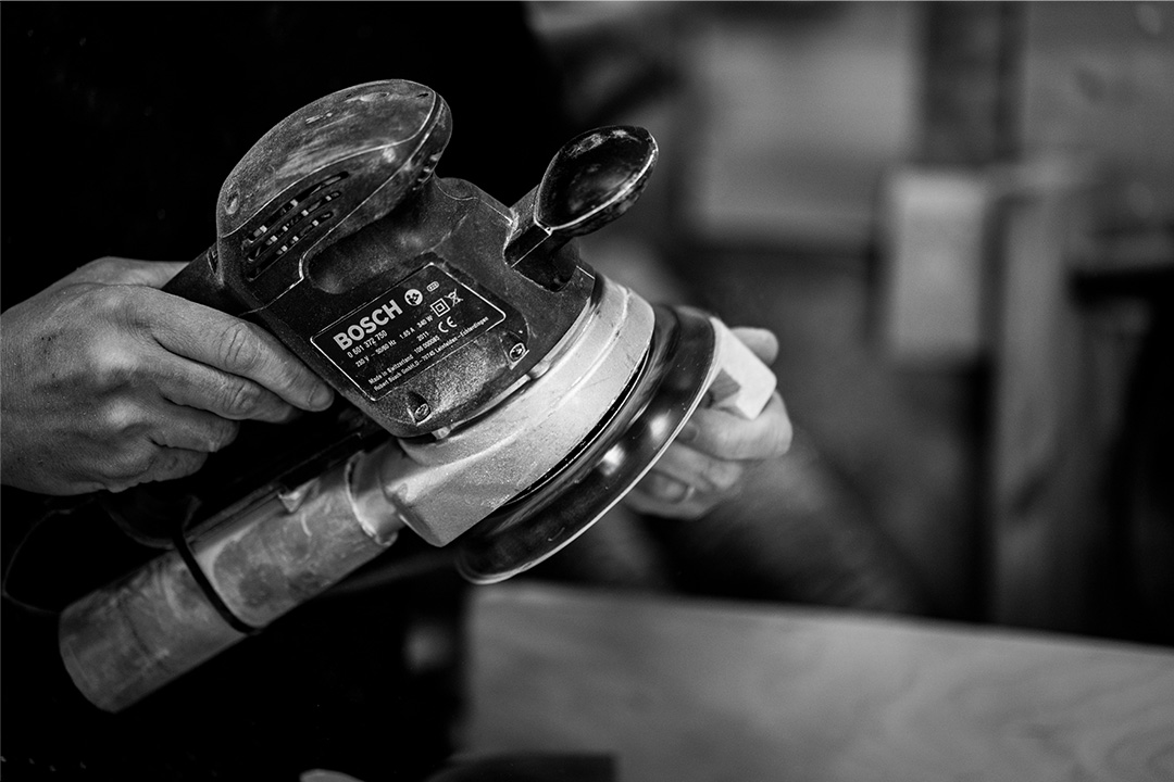 Photo en noir et blanc d'une personne à l'œuvre avec une ponceuse, mettant en avant l'effort et la technique.