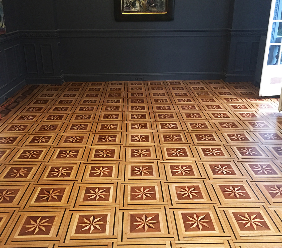 Une pièce avec un sol en bois au motif luxueux et authentique et une peinture accrochée au mur, créant une ambiance chaleureuse et artistique.