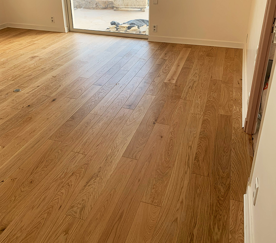 Intérieur d'une pièce spacieuse avec un large fenêtre et un parquet en bois, offrant une belle lumière naturelle.