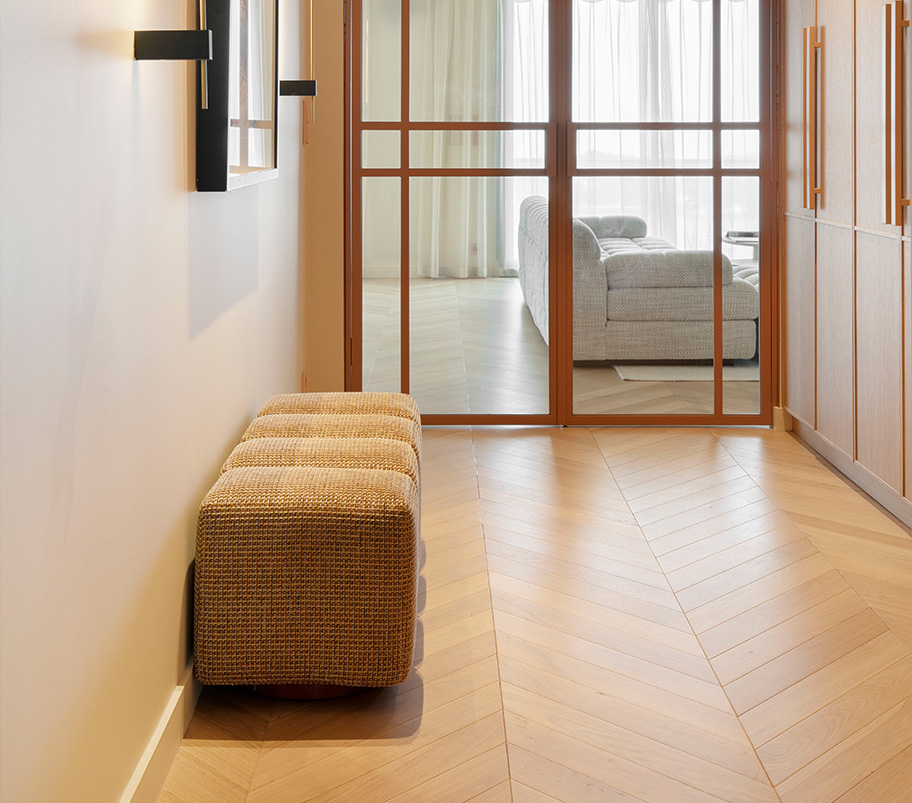 Un couloir avec un banc, une porte menant à un salon moderne et chaleureux, et du parquet au sol créant une atmosphère accueillante et fonctionnelle.