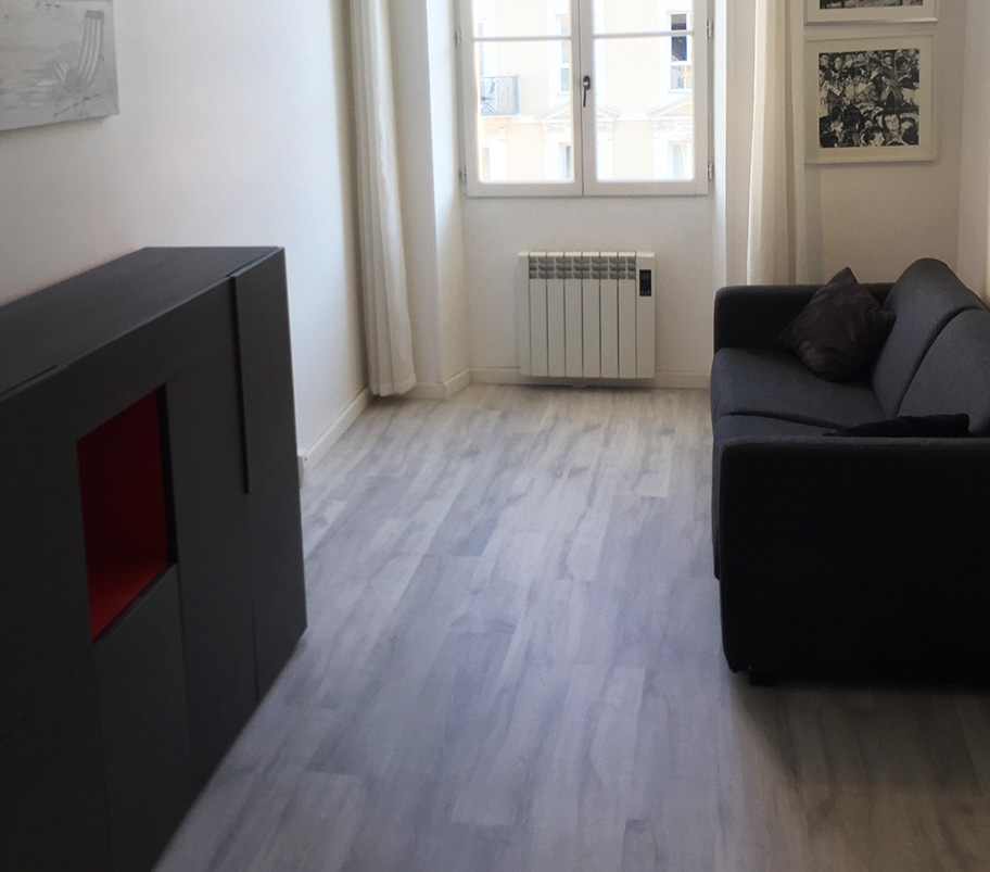 Intérieur d'un salon avec un canapé élégant et une télévision, et un sol en apparence bois, offrant une atmosphère chaleureuse et relaxante.