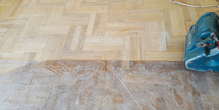 Passage d'une ponçeuse sur un parquet en bois naturel, mettant en avant l'aspect du bois avant et après ponçage