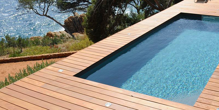 Une piscine au soleil entourée d'une terrasse en bois avec vue sur la mer
